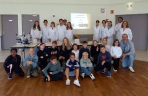 Students and scientists in lab coats, in a room  around a microscope