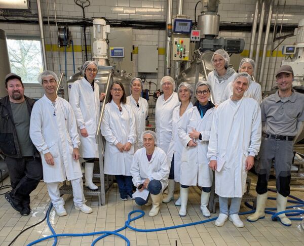 A group of people wearing white coats pose in a dairy technology laboratory.