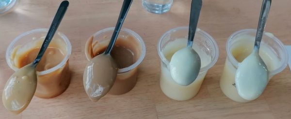 4 open yoghurt or cream dessert pots, with a spoon on top of each one